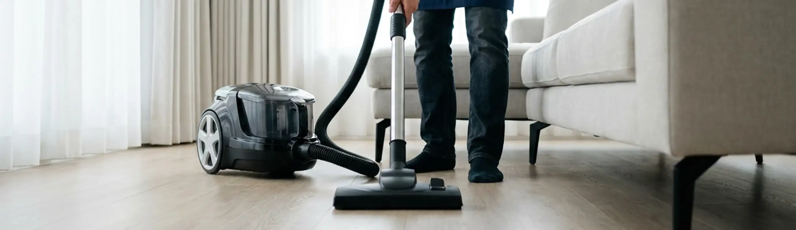 Professional house cleaner vacuuming a living room floor with a canister vacuum cleaner, Myrtle Beach, SC.