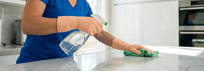 Maid service worker spraying and wiping a kitchen countertop with a microfiber cloth for sanitizing, Myrtle Beach, SC.