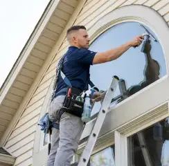 Professional window cleaner on a ladder using a squeegee to clean an exterior arched window, Myrtle Beach, SC.