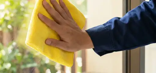 House cleaner wiping a glass window with a yellow microfiber cloth for streak-free cleaning, Myrtle Beach, SC.